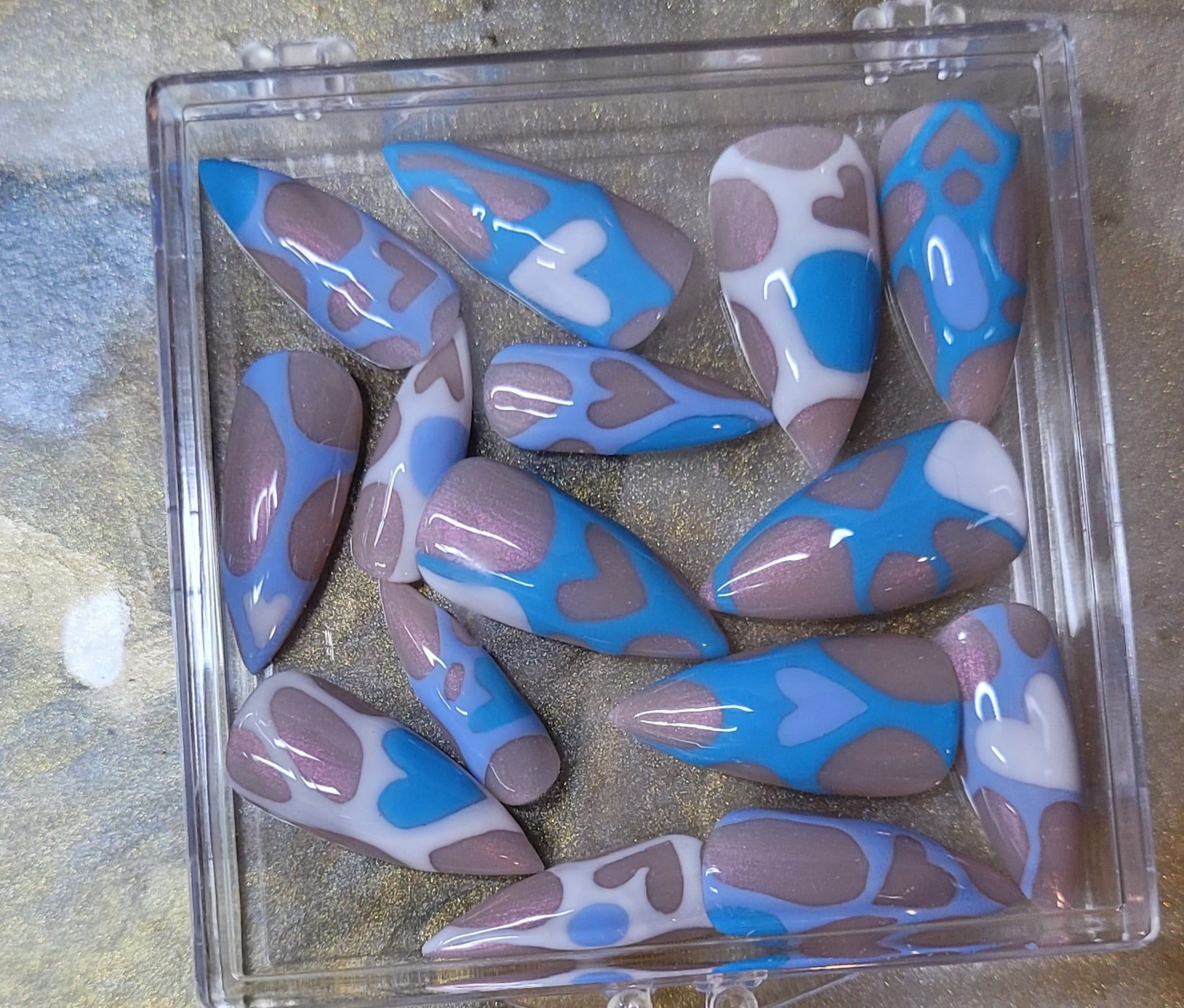 Set of blue and white nail tips in a clear plastic case on a textured surface.