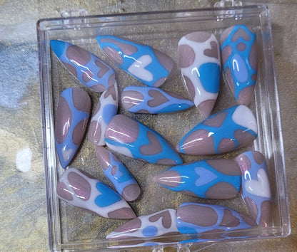 Set of blue and white nail tips in a clear plastic case on a textured surface.