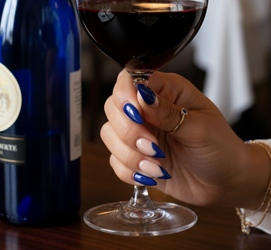 Hand holding a glass of red wine next to a bottle on a table in a restaurant setting.